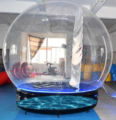 Water filled base Snow globe Large transparent inflatable dome with a blue base, set in a indoor space.